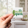 A hand holding a square magnet with a cartoon image of a pickle and the text "Pickle queen" on it.