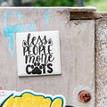 A sticker with the text "less people more cats" is attached to a concrete surface.