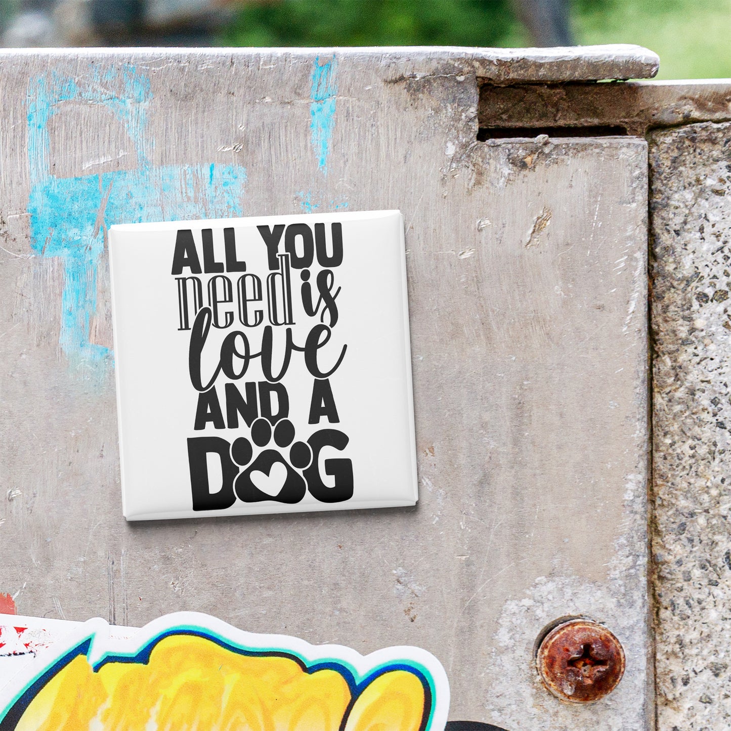 A white sticker with black text that says "ALL YOU NEED IS LOVE AND A DOG" is attached to a concrete surface.