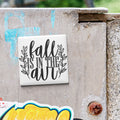 a white tile with the text "fall is in the air" written on it, which is attached to a concrete wall.