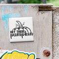 a white square tile with a black graphic and text that says "HEY THERE PUMPKIN" on a gray wall.