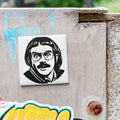 a sticker of a man's face with glasses and a mustache, placed on a weathered concrete surface.