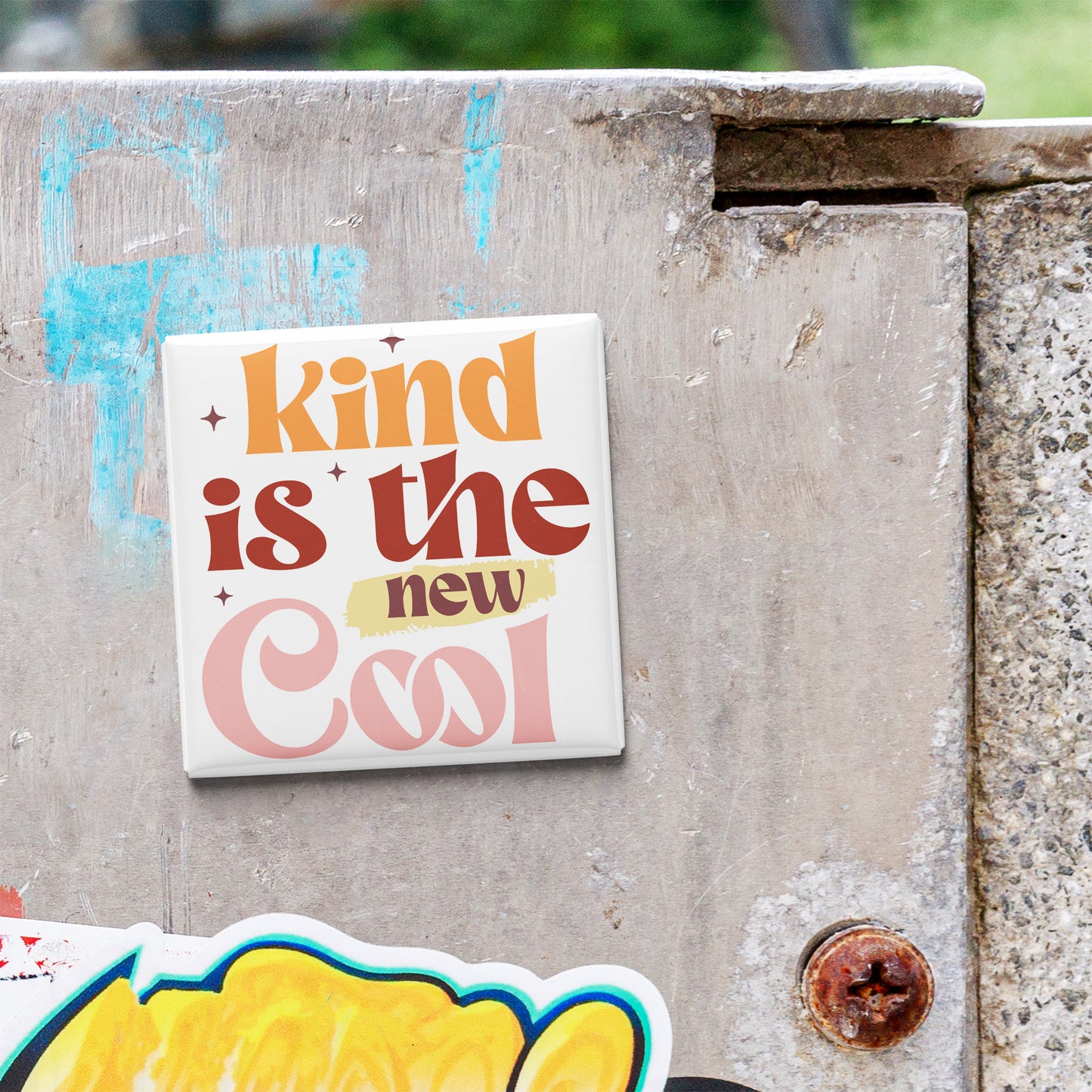 a sticker with the text "kind is the new cool" on a concrete wall.