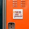 a vibrant orange wall with a white square sticker that reads "own your power".