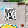 A white sign with black text that says "HAPPY FALL Y'ALL" is attached to a concrete wall.
