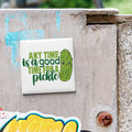 A sticker with a cartoon pickle and the text "Any time is a good time for a pickle" is attached to a concrete surface.