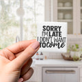A hand holding a small white object with black text that says "SORRY I'M LATE I DIDN'T WANT TO COME".