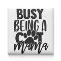 the text "BUSY BEING A COT MAMA" in a stylized font, with a paw print symbol replacing the letter "C".