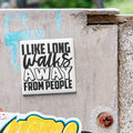 a sticker with the text "I LIKE LONG WALKS AWAY FROM PEOPLE" on a concrete surface.