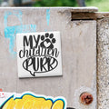A sticker with the text "My children purr" is attached to a concrete surface.