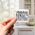 A hand holding a small white tile with the text "Pumpkin spice everything" written on it.