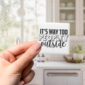 A hand holding a small white object with the text "IT'S WAY TOO PEOPLEY OUTSIDE" written on it.