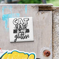 A sticker with the text "CAT HAIR is my glitter" is attached to a concrete surface.