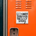 a sign with the text "100% NOT LEAVING THE HOUSE TODAY" on an orange surface, which appears to be a locker or a storage unit.