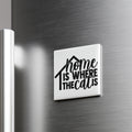 A white square magnet with the text "home is where the cat is" printed on it, mounted on a metallic surface.