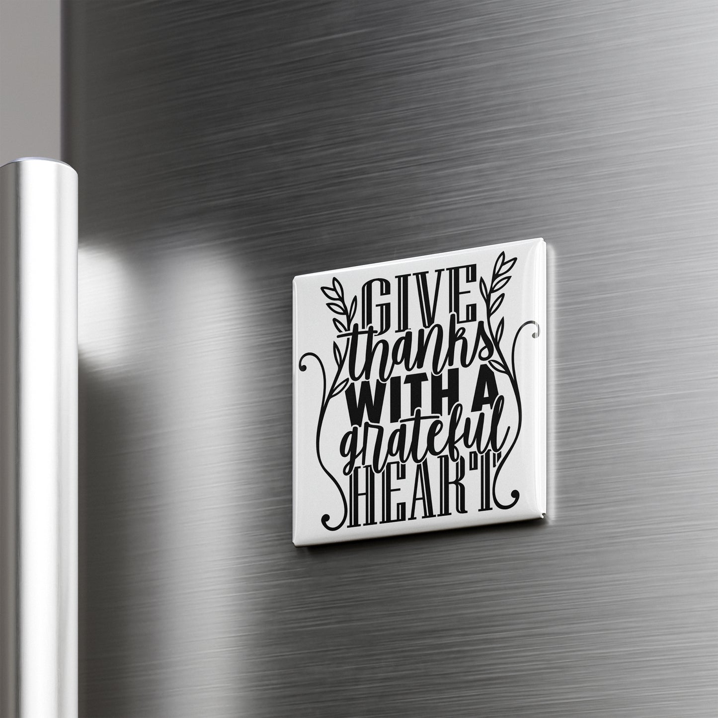 A white square magnet with a black text design that says "GIVE THANKS WITH A GRATEFUL HEART" attached to a metallic surface.