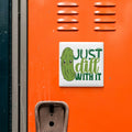 a sticker with a cartoon pickle and the text "Just dill with it" on an orange surface.