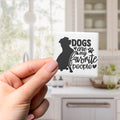 A hand holding a small square magnet with a black silhouette of a dog and the text "Dogs are my favorite people" printed on it.