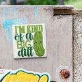 A sticker with a cartoon pickle and the text "I'm kind of a big dill" is attached to a concrete wall.