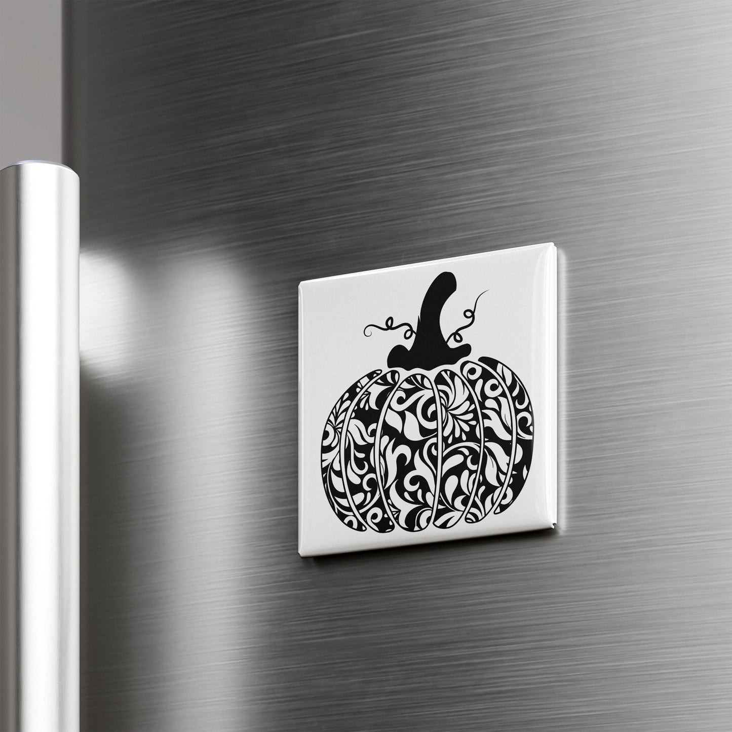 A decorative white square magnet with a black and white pumpkin design on it, mounted on a metallic surface.