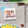 a sticker with the text "own your power" on a concrete surface.