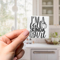 A hand holding a small white sticker with black text that says "I'm a fall kinda girl".