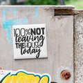 a sticker with the text "100% NOT LEAVING THE HOUSE TODAY" on a concrete surface.