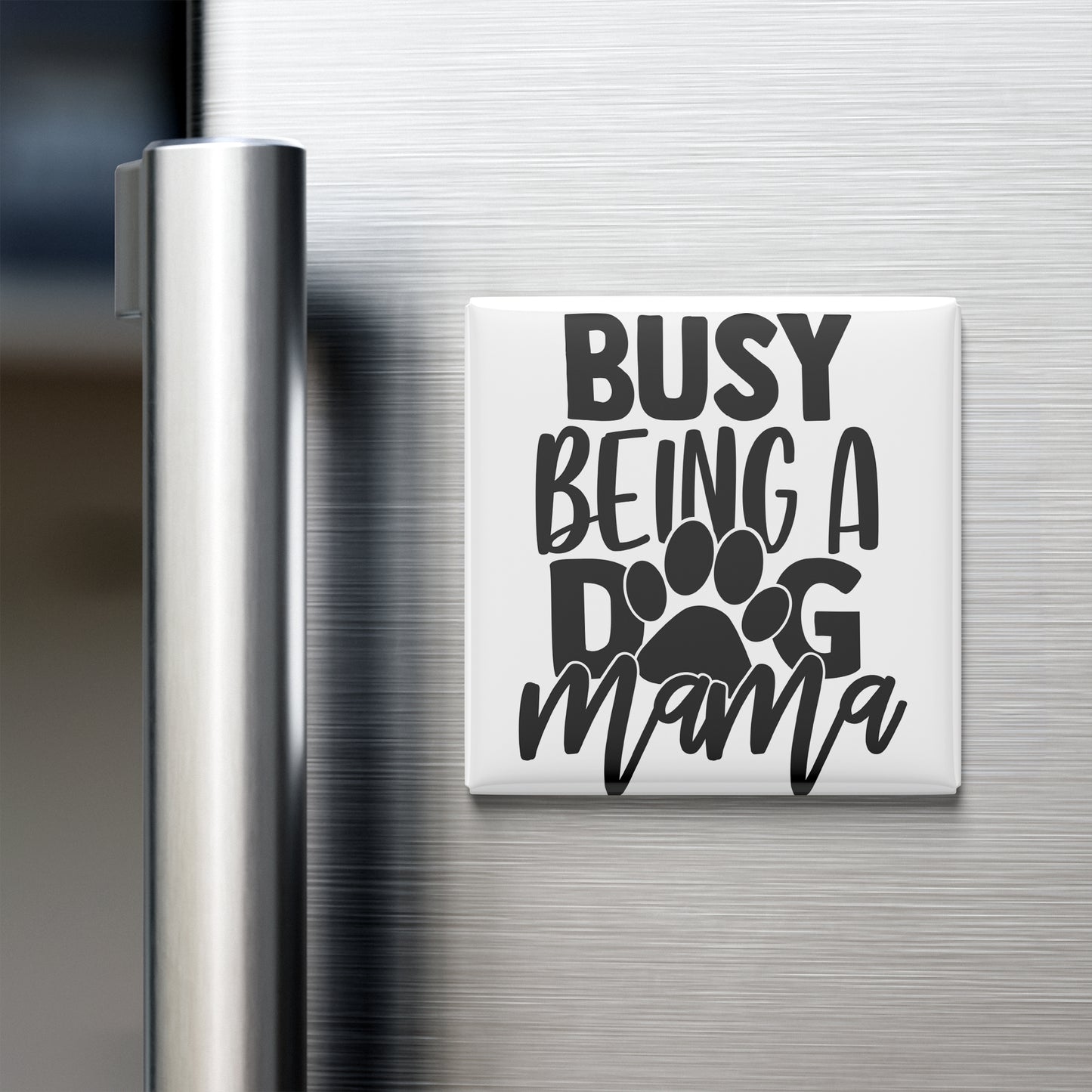 A white refrigerator magnet with the text "BUSY BEING A DOG MAMA" printed on it.