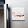 a white magnet with the text "kindness is magic" written on it, placed on a stainless steel refrigerator door.