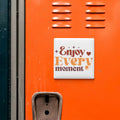 a vibrant orange wall with a motivational quote in the center, which reads "Enjoy Every moment".