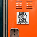 a sticker with the text "BUSY BEING A COT MAMA" on an orange surface, which appears to be a locker or a storage unit.