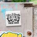 A sticker with the text "Yes I Really Do Need All These Dogs" is attached to a concrete surface.