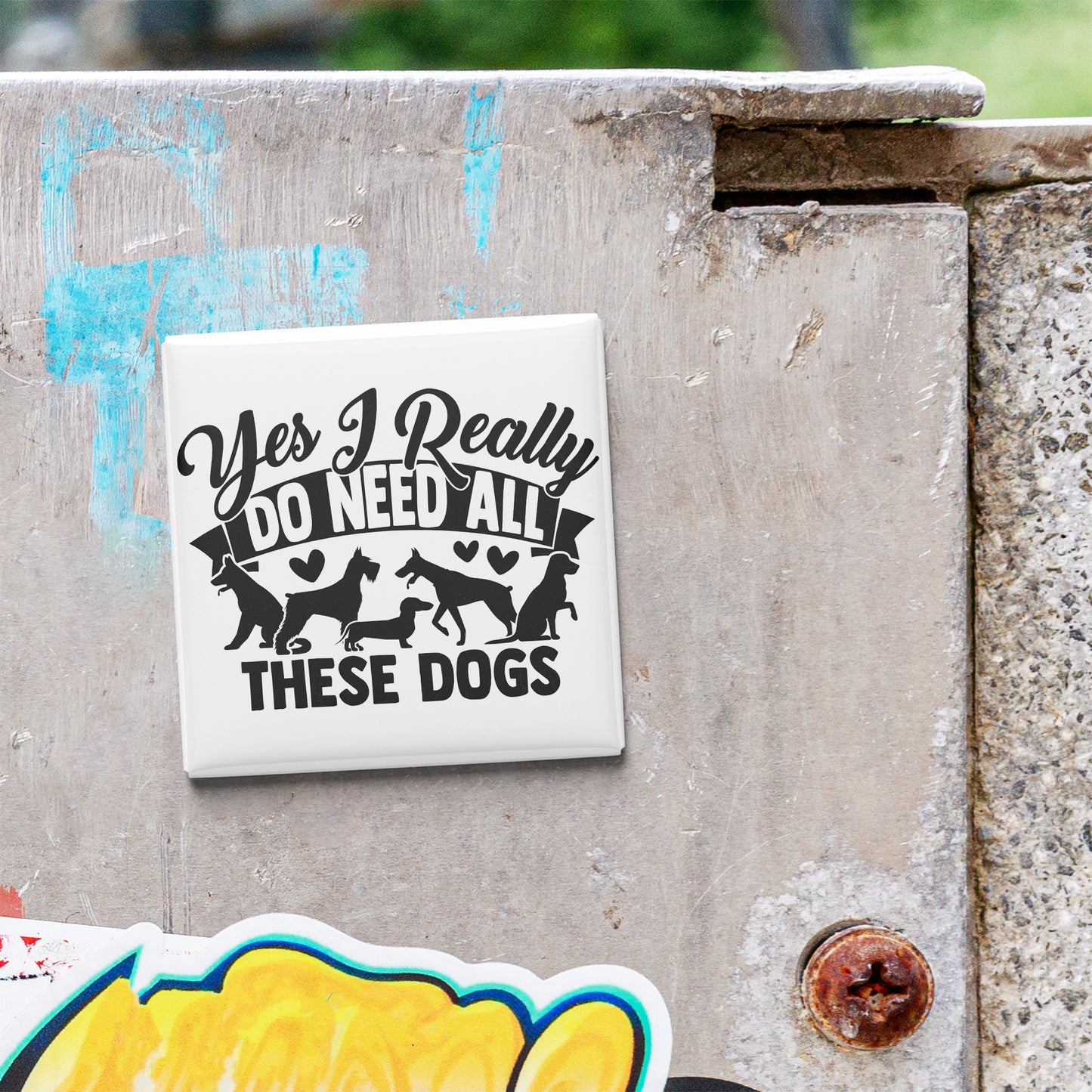 A sticker with the text "Yes I Really Do Need All These Dogs" is attached to a concrete surface.