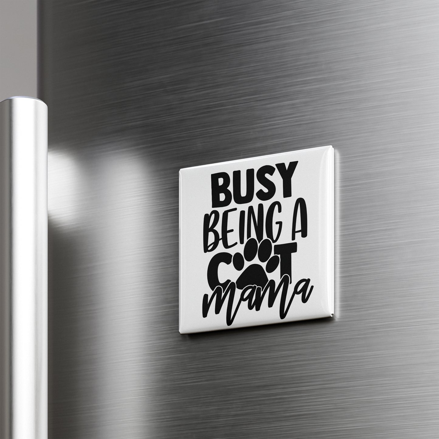 A white refrigerator magnet with the text "BUSY BEING A COT MAMA" printed on it.