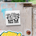 A sticker with the text "Yes I Really Do Need All These Cats" is attached to a concrete surface.