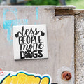 A sticker with the text "less people, more dogs" is attached to a concrete surface.