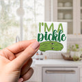 A hand holding a sticker with a cartoon image of a pickle and the text "I'm a pickle" printed on it.