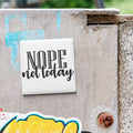 a white square magnet with the text "NOPE not today" written on it, which is attached to a weathered concrete surface.