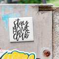 a white square magnet with the text "Stay Home Club" written on it, placed on a weathered concrete surface.