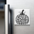 A decorative pumpkin magnet is attached to the side of a stainless steel refrigerator.