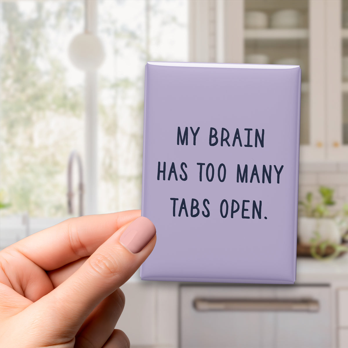 Hand holding the 2.5 × 3.5-inch “My brain has too many tabs open.” magnet in a kitchen