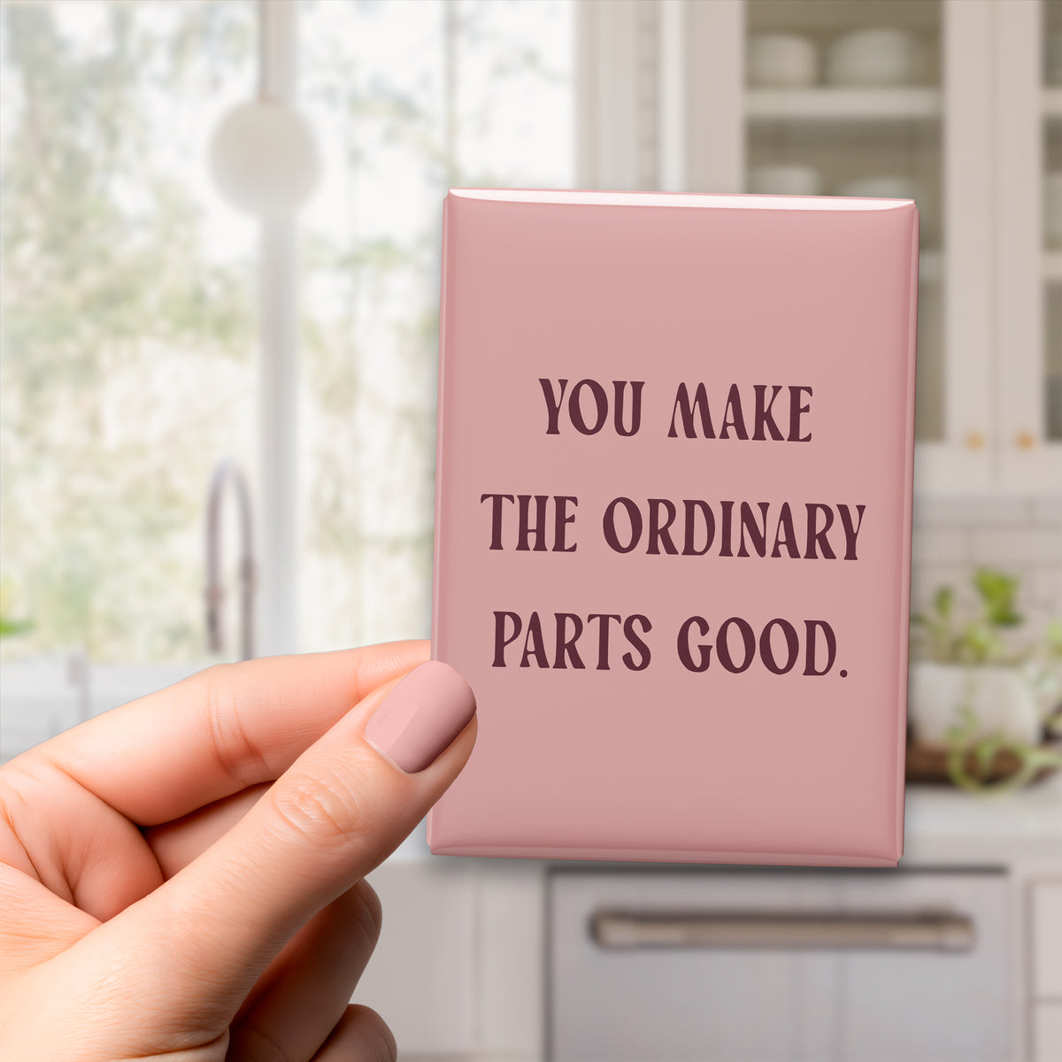 Hand holding the 2.5 × 3.5-inch “You make the ordinary parts good.” magnet in a kitchen