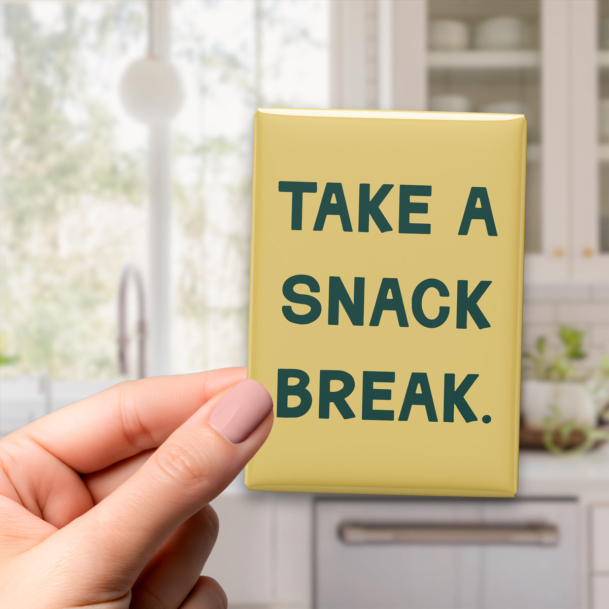 Hand holding the 2.5 × 3.5-inch “Take a snack break.” magnet in a kitchen