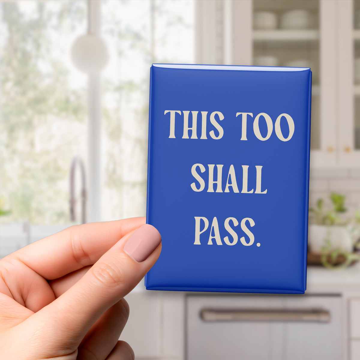 Hand holding the 2.5 × 3.5-inch “This too shall pass.” magnet in a kitchen