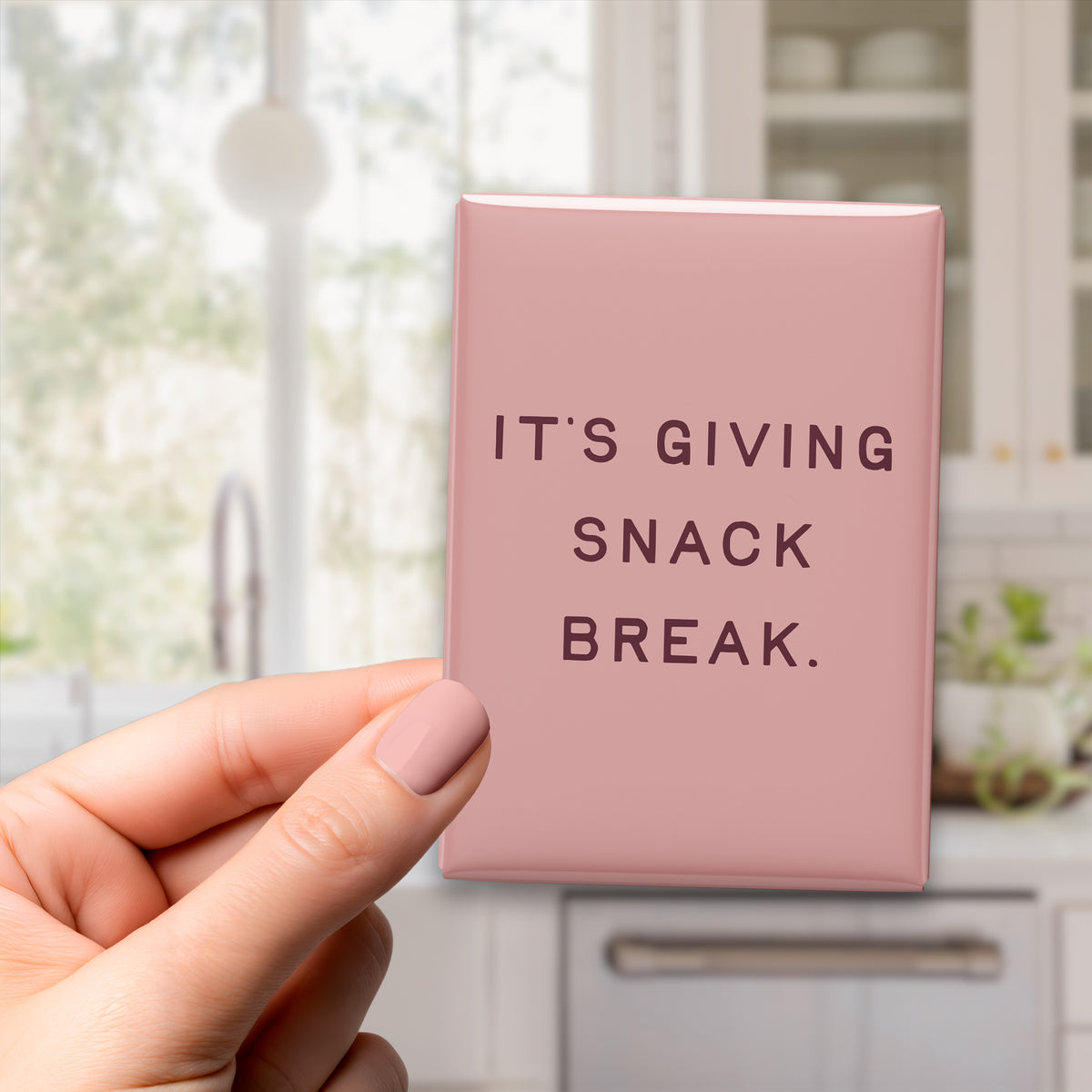 Hand holding the 2.5 × 3.5-inch “It's giving snack break.” magnet in a kitchen