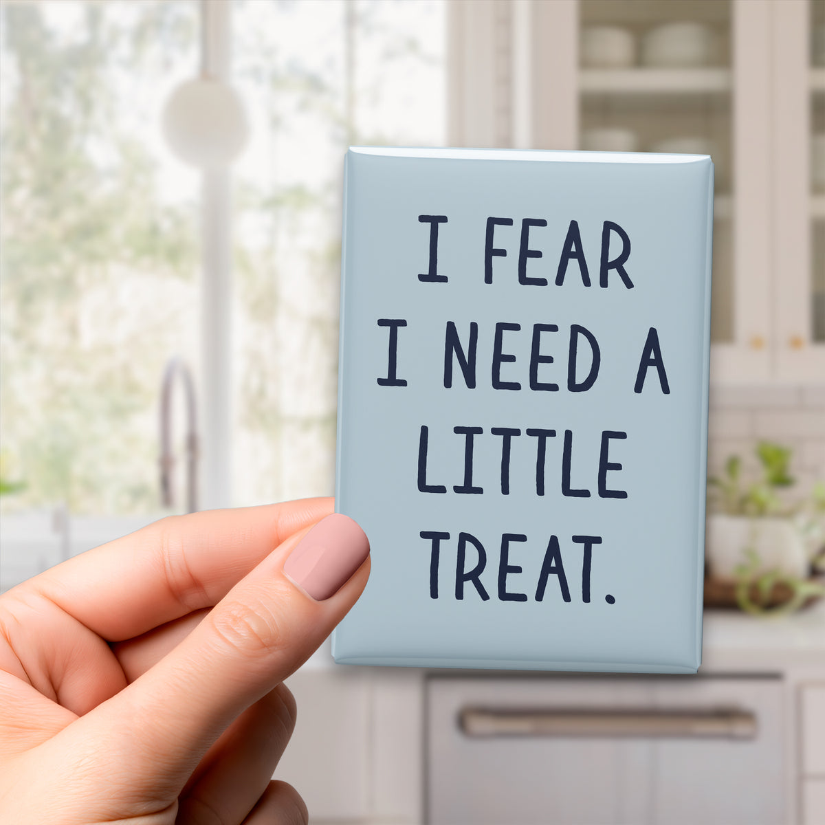 Hand holding the 2.5 × 3.5-inch “I fear I need a little treat.” magnet in a kitchen