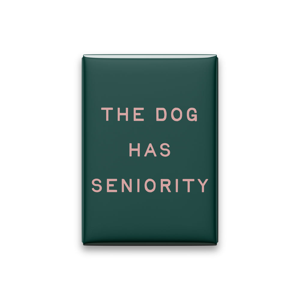 The Dog Has Seniority magnet in Blush lettering on a Spruce background, shown on white