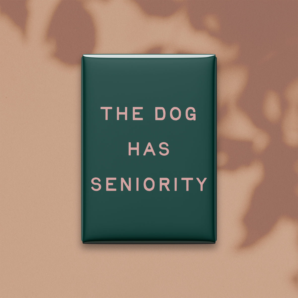 The Dog Has Seniority magnet in Blush lettering on a Spruce background, shown on a warm neutral background