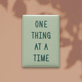 One Thing at a Time magnet in Spruce lettering on a Sage background, shown on a warm neutral background