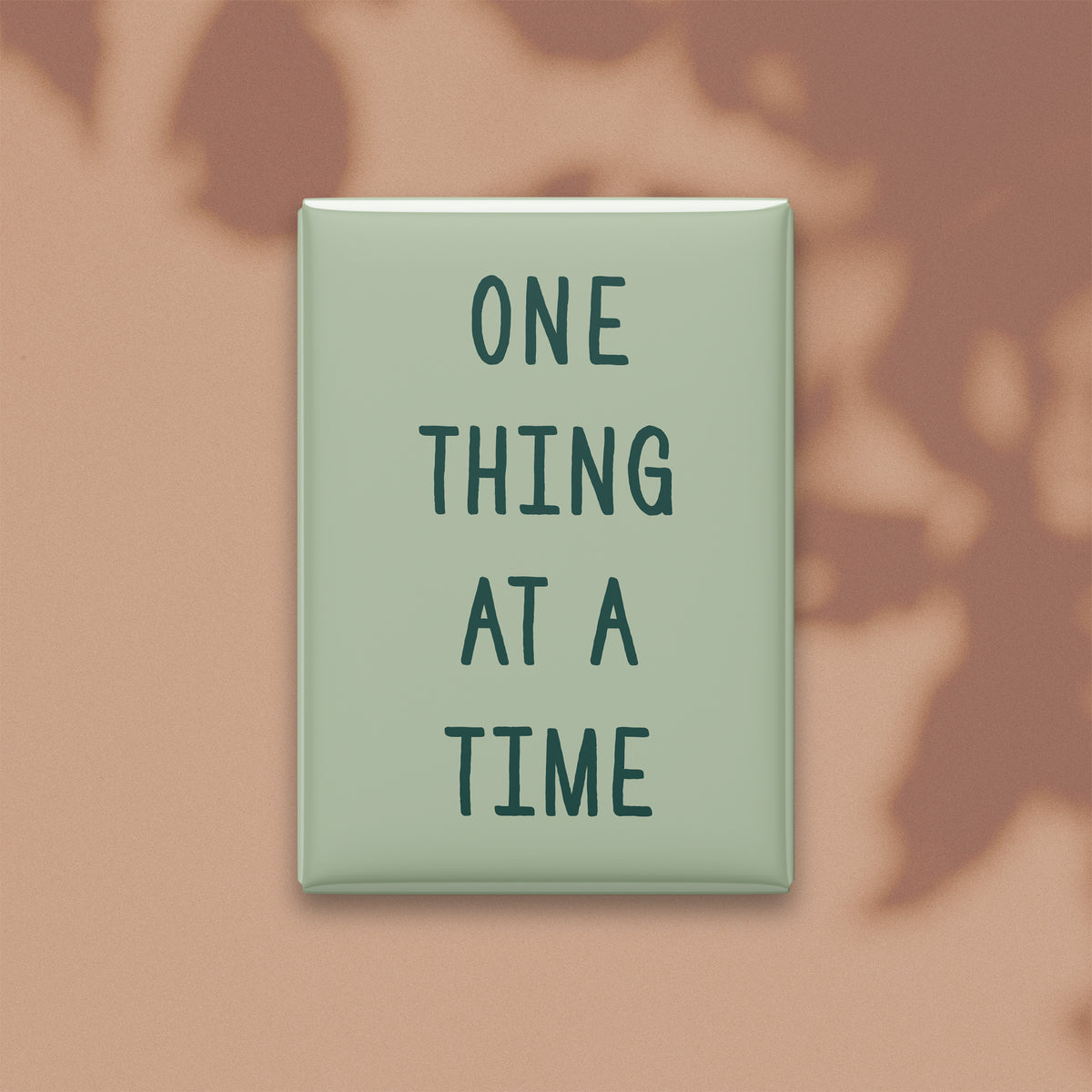 One Thing at a Time magnet in Spruce lettering on a Sage background, shown on a warm neutral background